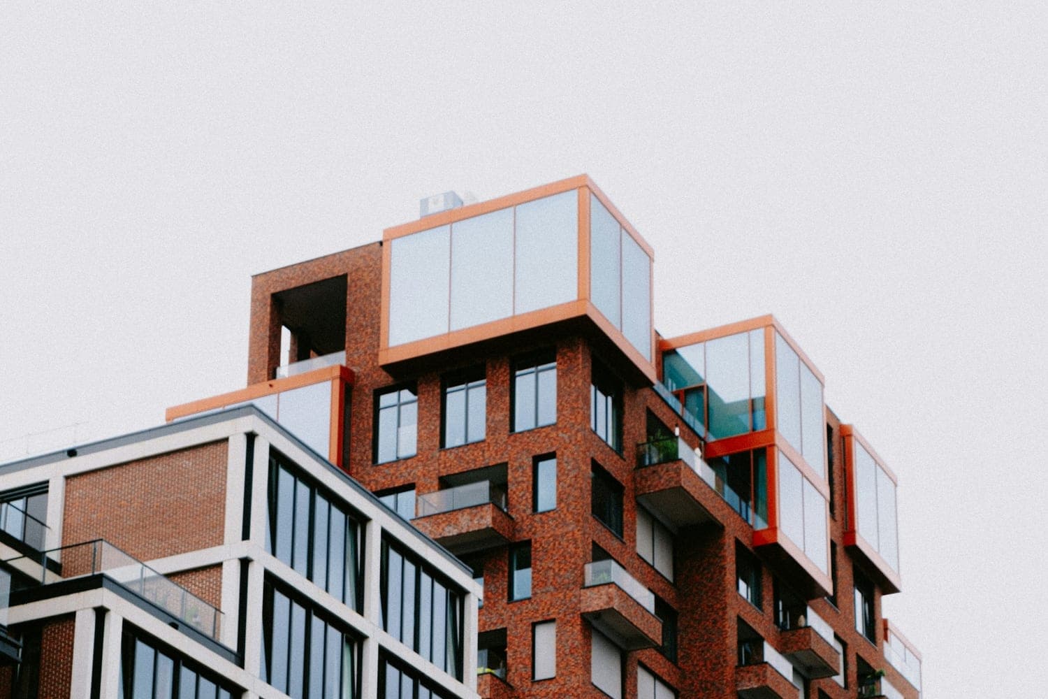 Een modern appartementengebouw van rode baksteen met uitstekende glazen serres en balkons.